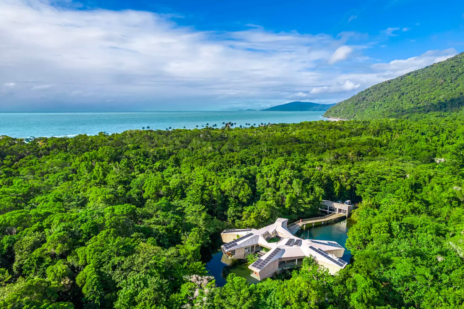 Aerial view of Alkira Resort House at Cape Tribulation, an architectural off-grid residence surrounded by its lagoon and rainforest, with the Coral Sea beyond